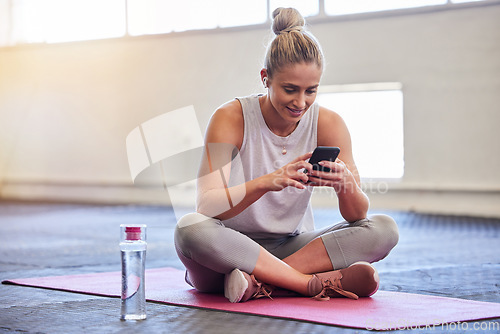 Image of Exercise, relax and woman with phone on floor reading email or text after yoga workout at gym. Health, pilates and technology, girl on ground with smartphone checking fitness app online siting on mat