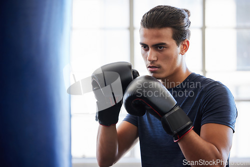 Image of Man, boxing and fitness in gym exercise for power, performance and cardio against a window background. Boxer, fighter and athletic male training on punching bag at sports center, serious and tough