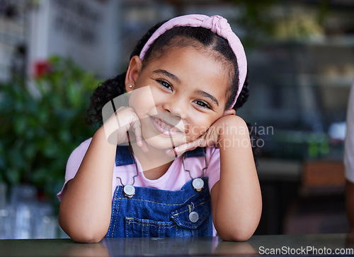 Image of Black child, face and girl portrait with a smile, happiness and cute clothes with hands for headshot. Happy kid at a table for fashion, positive mindset and blurred background at cafe or home