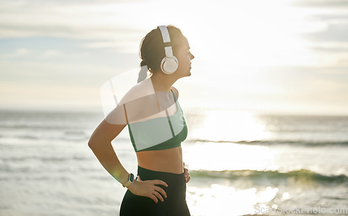 Image of Sunshine headphones and woman on beach, fitness and streaming music for peace, balance or resting. Female, lady or confident athlete with headset, sunlight or seaside for running, workout or exercise