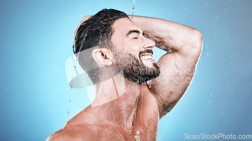 Image of Face skincare, water splash and man in shower in studio isolated on a blue background. Wellness, dermatology and happy male model cleaning, washing and bathing for healthy skin, self care and hygiene