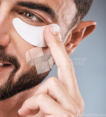 Image of Skincare, face and man with eye patch in studio isolated on a gray background for wellness. Thinking, dermatology and male model with cosmetics, facial treatment or mask product for healthy skin.