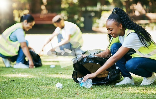 Image of Volunteer group, nature park and cleaning for community service for clean environment, recycling and pollution. Black woman happy to help people with plastic bottle and trash bag outdoor green grass