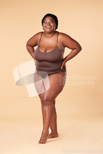 Image of Portrait, happy or plus size with a model black woman posing hands on hips in studio on a beige background. Wellness, underwear and smile with a female standing proud or confident for body positivity