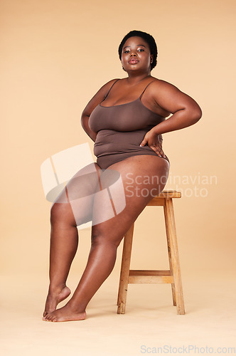 Image of Portrait, beauty and plus size with a model black woman posing on a chair in studio on a beige background. Wellness, underwear and natural with a female sitting on a stool for body positivity