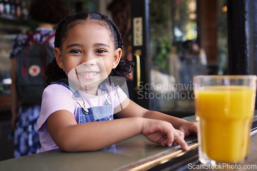 Image of Happy, smile and portrait of a child at a restaurant for food, breakfast and juice. Playful, happiness and girl sitting in a cafe, coffee shop or store for lunch, dinner or meal with a drink