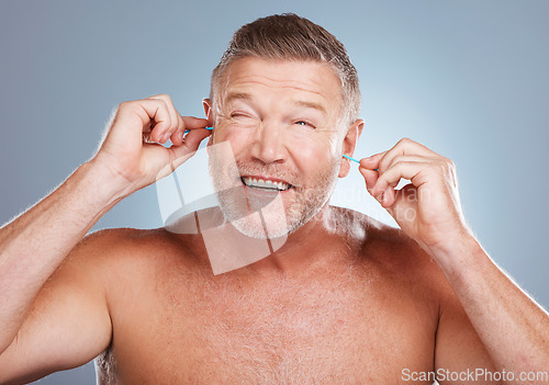 Image of Earbuds, health and man cleaning his ears in a studio for self care and funny hygiene. Beauty, wellness and healthy mature guy doing his morning grooming routine isolated by a gray background.
