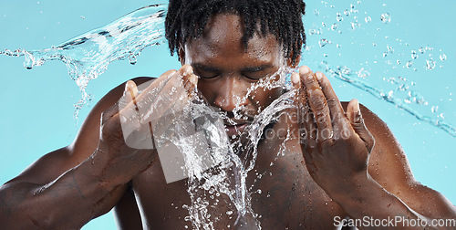 Image of Water, splash and cleaning face for hygiene with a model black man in studio on a blue background for hydration. Bathroom, skincare or wellness with a male washing himself for natural skin treatment