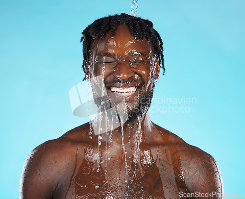 Image of Water drops, skincare and black man isolated on blue background for face cleaning, body shower and smile. Strong, beauty model or person, facial glow in studio headshot washing or dermatology hygiene
