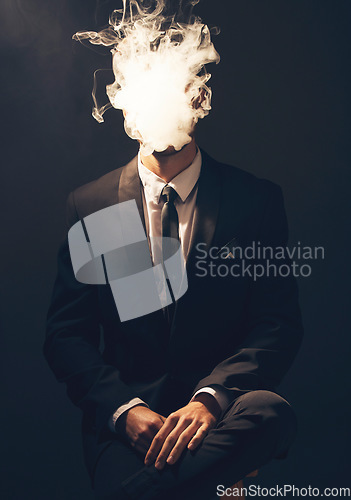 Image of Businessman, suit and smoke in dark studio for corporate fashion, mafia aesthetic and success. Young model, man and smoking to hide face in secret for crime boss, vintage hand by black background