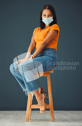 Image of Covid, model mask portrait and woman sitting on a chair with casual fashion in a studio. Isolated, gray background and young model with marketing space for mockup feeling beautiful and happiness