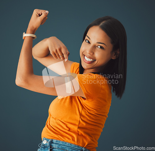 Image of Vaccine, plaster and portrait of a woman in a studio with a strength gesture after being vaccinated. Happy, smile and proud female model with a vaccination band aid isolated by a dark blue background