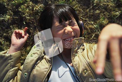 Image of Funny, playful and girl with headphones on grass for freedom, comedy and crazy in Singapore. Summer, comic and Asian child lying in park to relax, streaming music and lisrening to audio while playing