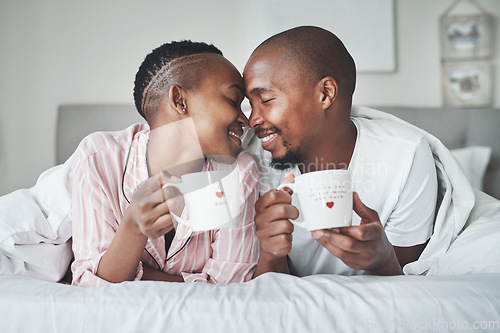 Image of Love, valentines day and black couple gift cups lying in bed in the morning drinking coffee in the bedroom together. Kiss, romantic and happy lovers relax in a home, house or apartment on holiday