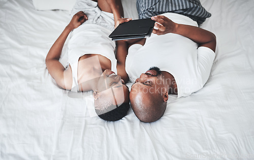 Image of Black couple, tablet and relax on bed with smile for entertainment, browsing or social media at home. Happy African American man and woman relaxing in bedroom on touchscreen for morning streaming