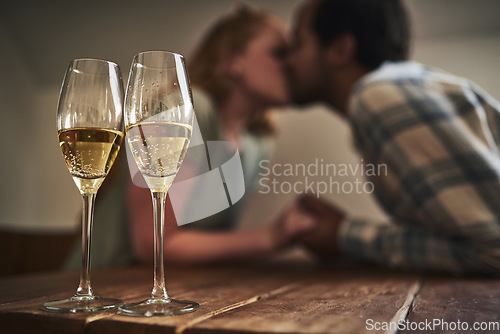 Image of Champagne, glasses and love on valentines day with a couple kissing in the background of a restaurant for romance. Alcohol, drink or dating with a man and woman sharing a kiss on a romantic date