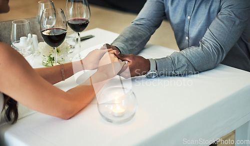 Image of Love, date and couple holding hands in restaurant for romantic dinner, celebration and anniversary. Interracial relationship, fine dining and man and woman have drinks or wine on Valentines day