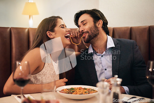 Image of Date, laughing and playful couple eating spaghetti on a romantic dinner at a restaurant and enjoying a meal. Lovers, man and woman playful with pasta, food or a meal on valentines day and in love