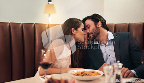 Image of Happy couple, sharing food and kiss for dinner date, embrace or relationship romance at night in restaurant. Man and woman lean with noodle mouth for intimate kissing in fine dining on valentines day