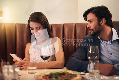 Image of Cellphone, chatting and couple on a date at a restaurant for valentines day, romance or anniversary. Communication, upset and annoyed man watching his happy girlfriend sitting on her phone at dinner.