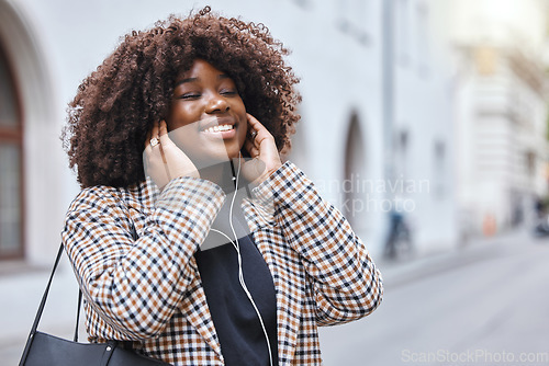 Image of Happy, city and black woman listening to music, radio or song in the street while walking to work. Happiness, smile and African female streaming a playlist, album or audio with earphones in the road.