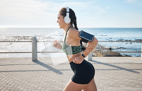 Image of Music, fitness and woman at beach for running, exercise and morning cardio on blue sky background. Radio, podcast and workout run by girl at ocean for training, happy or relax with audio motivation