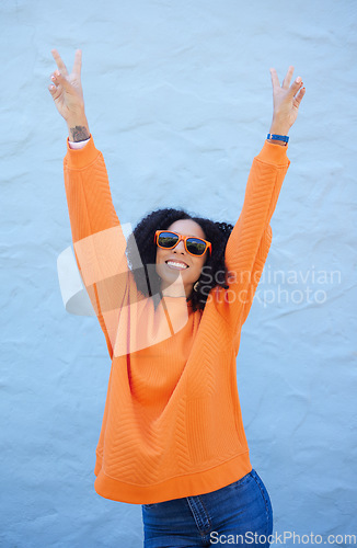 Image of Carefree, peace sign and trendy woman on a wall in the city for cool energy, playful and happy with sunglasses. Comic, fun and crazy stylish girl with a hand emoji for freedom and funky smile