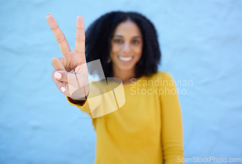 Image of Black woman, hand and peace sign for victory, win or letter V against a blue wall background on mockup. Hand of happy African American female winner smiling showing peaceful symbol, gesture or emoji