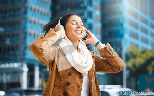 Image of Black woman, headphones and listening to music in city for travel, motivation and happy mindset. Young person on an urban street with buildings background while streaming podcast or audio outdoor