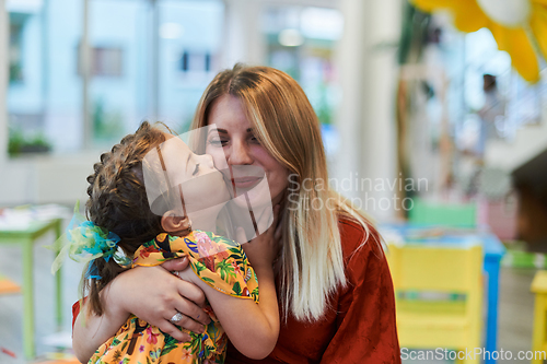 Image of A cute little girl kissing and hugs her mother in preschool