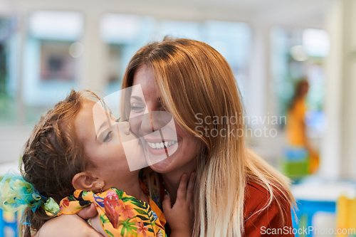 Image of A cute little girl kissing and hugs her mother in preschool