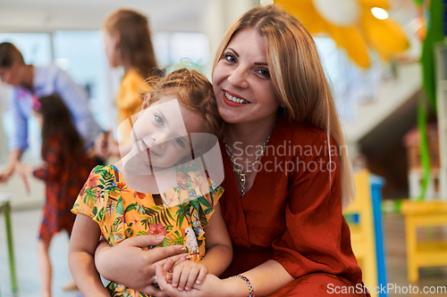 Image of A cute little girl kissing and hugs her mother in preschool