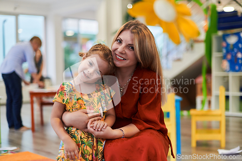 Image of A cute little girl kissing and hugs her mother in preschool