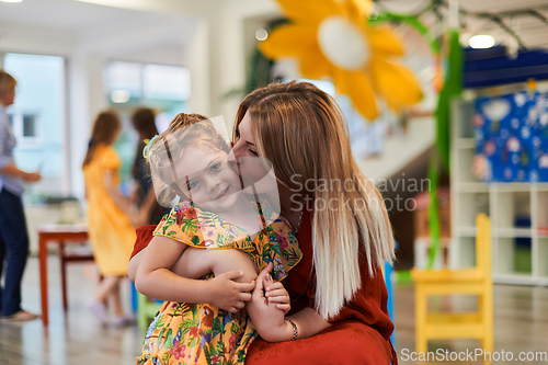 Image of A cute little girl kissing and hugs her mother in preschool