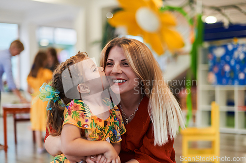 Image of A cute little girl kissing and hugs her mother in preschool