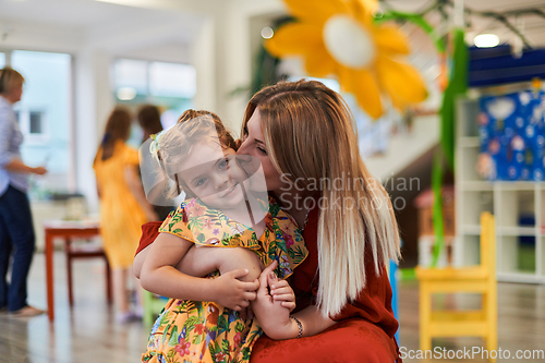 Image of A cute little girl kissing and hugs her mother in preschool