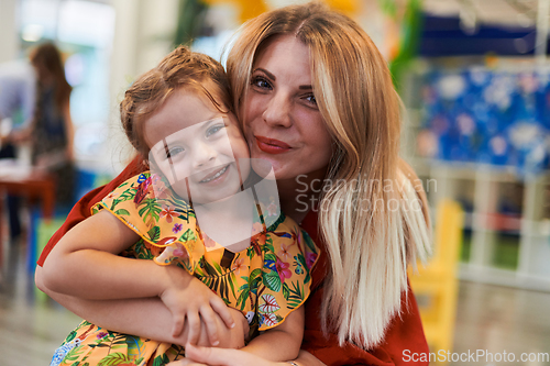 Image of A cute little girl kissing and hugs her mother in preschool