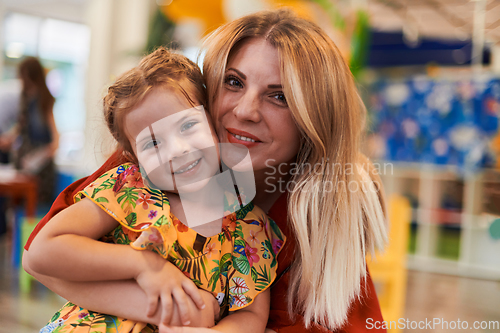 Image of A cute little girl kissing and hugs her mother in preschool