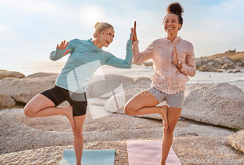 Image of Women friends, beach yoga and happy in morning with stretching pose for health, wellness and helping hand. Black woman, fitness group and laugh for comic moment with balance, peace and support by sea