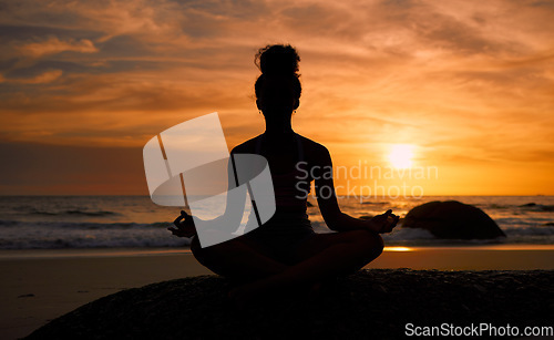 Image of Sunset, beach and silhouette of a woman in a lotus pose while doing a yoga exercise by the sea. Peace, zen and shadow of a calm female doing meditation or pilates workout outdoor at dusk by the ocean