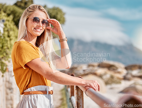 Image of Portrait, beach and fashion with a woman outdoor in nature by the ocean or sea in the summer season. Travel, freedom and happy smile with a young female standing outside on a coastal shoreline