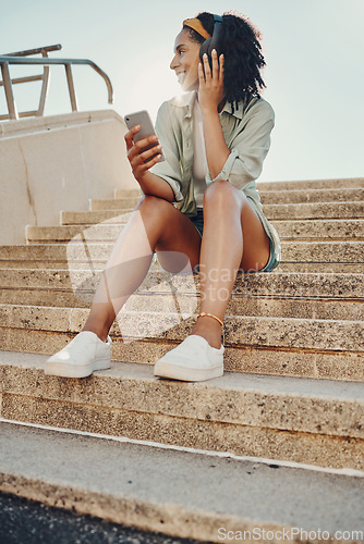 Image of Black woman in city, smartphone and headphones for music, travel and 5g network for audio streaming outdoor. Happy person in Miami, listen to radio or podcast, relax on steps with internet and urban