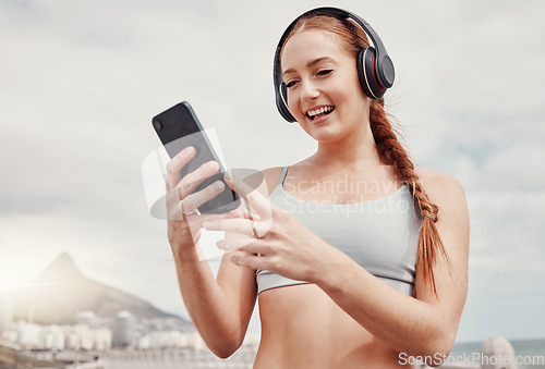 Image of Headphones, phone and woman doing workout in the city while listening to music, podcast or radio. Fitness, wellness and female athlete networking on social media with cellphone after outdoor exercise