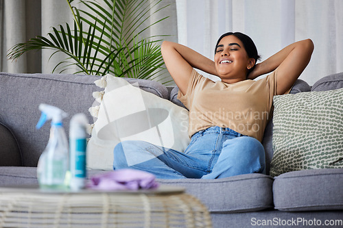 Image of Woman, relax and sofa after cleaning house with smile, satisfaction and pride in home living room. Cleaner, rest and happy on lounge couch with spray, cloth and hygiene product on table in apartment