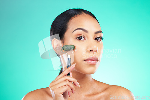 Image of Portrait, jade roller and woman with face massage in studio for wellness, grooming or skincare on isolated blue background. Beauty, facial and massaging tool by girl model relax, skin or product