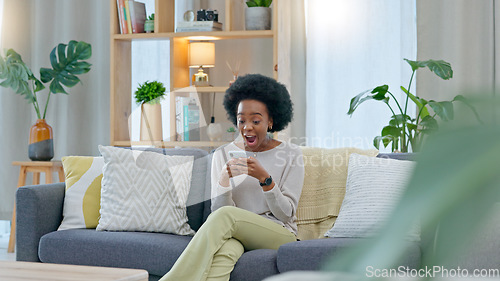 Image of African woman celebrating a new job while sitting at home on a couch. A young females loan is approved via an email on her phone. A happy and excited lady cheering for a promotion on a sofa