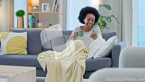 Image of Happy woman reading social media news on a phone while drinking coffee on a sofa at home. Young African American female texting and sharing interesting funny and humorous content on the internet