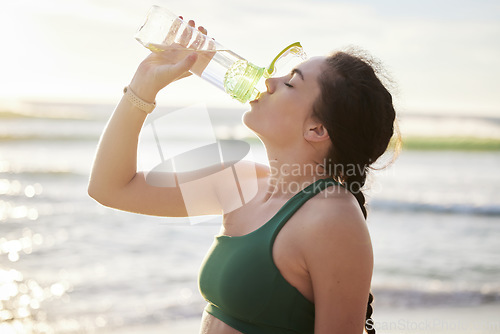 Image of Drinking water, beach and woman in fitness training, exercise or outdoor workout with nutrition, health and wellness. Liquid bottle for diet, goals and or cardio of runner, athlete or person by sea