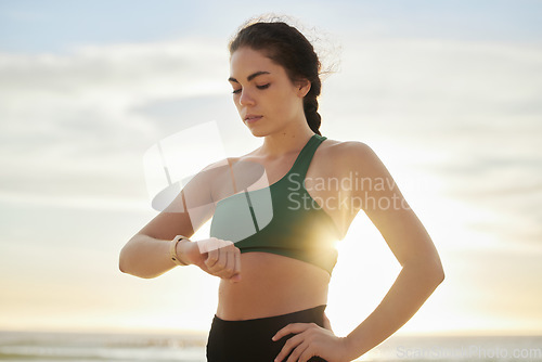 Image of Smart watch, woman and fitness at sunset on beach for exercise workout, training and nature. Stopwatch, sports and female at sea check time, heart rate and monitor healthy body progress for wellness