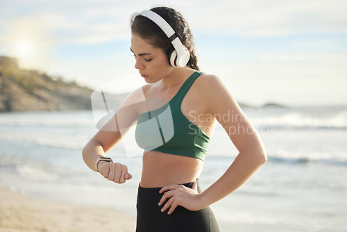 Image of Headphones, smartwatch and beach woman for workout, exercise or runner results, progress or wellness. Goals, check timer and mental health of sports person listening to music, podcast by sea or ocean